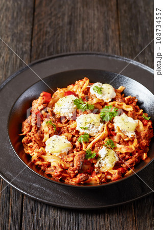 Lasagnette with beef ragu, mushrooms and ricotta cheese in black bowl on dark wooden table  108734557