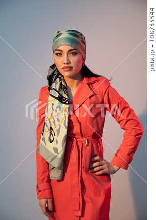 a woman in a headscarf in an orange dress stands indoors 108735544