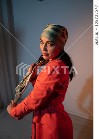 a woman in a headscarf in an orange dress stands indoors a woman in a headscarf in an orange dress stands indoors 108735547