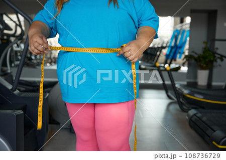 Closeup waistline of overweight woman wrapped in measuring tape Closeup waistline of overweight woman wrapped in measuring tape 108736729