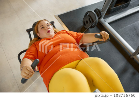 Chubby young woman enjoying leg training day at gym Chubby young woman enjoying leg training day at gym 108736760