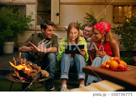 Happy teen friends spending evening nearby bonfire and campsite 108736775