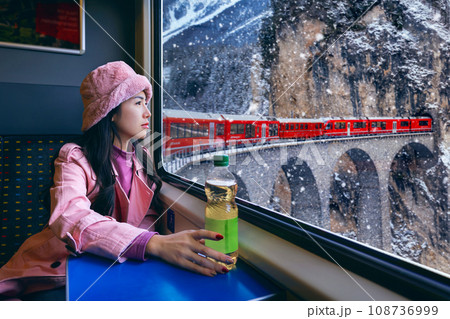 Tourist looking out the window enjoying with Train passing through famous mountain in Filisur, Switzerland. Landwasser Viaduct world heritage with train express in Swiss Alps snow winter scenery. 108736999