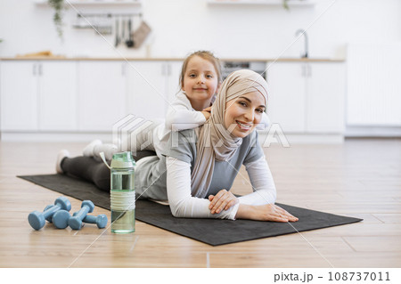 Muslim female in hijab relaxing with cute daughter after fitness routine at home 108737011