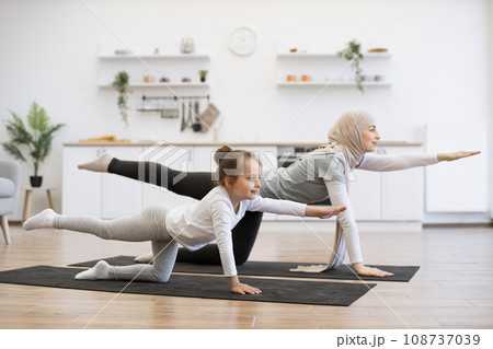 Beautiful mother with her girl practicing yoga exercise together in kitchen. Beautiful mother with her girl practicing yoga exercise together in kitchen. 108737039
