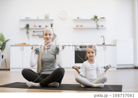 Happy young mom and baby girl exercising together with joy on mat at home. 108737081