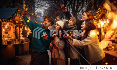Cozy winter fair. Young happy people, friends taking selfie together, drinking mulled wine, celebrating holidays outdoors 108738161