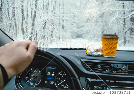 The steering wheel of a car, a hamburger and coffee on the dashboard, a winter road 108738711