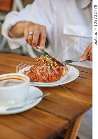 A woman enjoys a delicious breakfast of crisp croissants and coffee in cafe A woman enjoys a delicious breakfast of crisp croissants and coffee in cafe 108738779