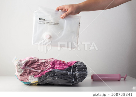 A man's hand holds vacuum bags for storing clothes and things on a white background. Pumping air out of bags with a hand pump, close-up 108738841