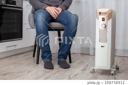 Modern electric heater in the kitchen against the background of a sitting man in a chair. Heater concept with automatic shutdown and thermostat. Heating the apartment in the autumn and winter, 108738912