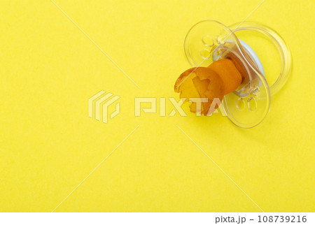 Low-quality torn baby silicone pacifier on a yellow background, close-up. Concept of the anatomical shape of the pacifier, teething in children. Copy space for text Low-quality torn baby silicone pacifier on a yellow background, close-up. Concept of the anatomical shape of the pacifier, teething in children. Copy space for text 108739216
