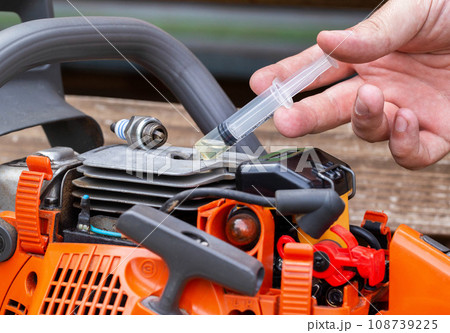 Injection of fuel from a syringe into the combustion chamber of a chainsaw. Checking the carburetor system and chainsaw ignition system. Close-up Injection of fuel from a syringe into the combustion chamber of a chainsaw. Checking the carburetor system and chainsaw ignition system. Close-up 108739225
