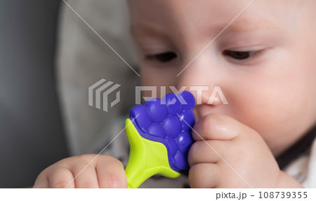 Handsome baby boy bites with his mouth a silicone massager with cooling for teeth gums. Teeth erupting in the gums. Pain and itching. Handsome baby boy bites with his mouth a silicone massager with cooling for teeth gums. Teeth erupting in the gums. Pain and itching. 108739355