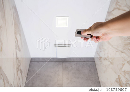A man holds in his hand an exhaust ventilation control panel and a light control in the bathroom. Copy space for text A man holds in his hand an exhaust ventilation control panel and a light control in the bathroom. Copy space for text 108739807