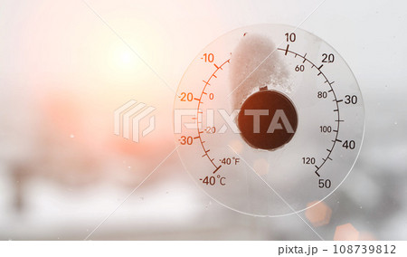 The rays of the setting sun in the sky against the background of a street thermometer with a snow cap on the window. Snowy weather and warming concept. Weather forecast Copy space for text 108739812