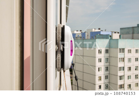 A modern vacuum robot window washer washes glass in an apartment on a balcony. View outside from the street. Safety from falls from a height. 108740153