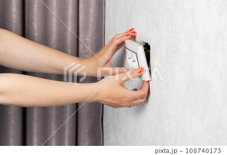 The girl is trying to insert a torn out socket from the socket due to the wrong pulling out of the electrical plug. Close-up, girl's hands with manicure. The girl is trying to insert a torn out socket from the socket due to the wrong pulling out of the electrical plug. Close-up, girl's hands with manicure. 108740173