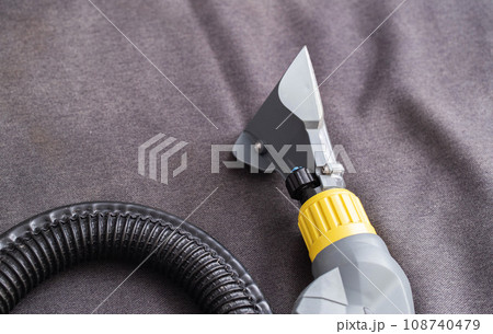 Washing vacuum cleaner with a special nozzle on the black upholstery of the sofa. Upholstered furniture cleaning service. Copy space for text Washing vacuum cleaner with a special nozzle on the black upholstery of the sofa. Upholstered furniture cleaning service. Copy space for text 108740479
