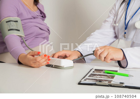 A pregnant girl at a doctor's appointment measures blood pressure. The concept of arterial hypertension and hypotension during pregnancy, preeclampsia. Copy space for text 108740504