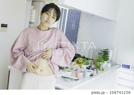 キッチンの前でお腹の脂肪を気にする若い女性 キッチンの前でお腹の脂肪を気にする若い女性 108741256