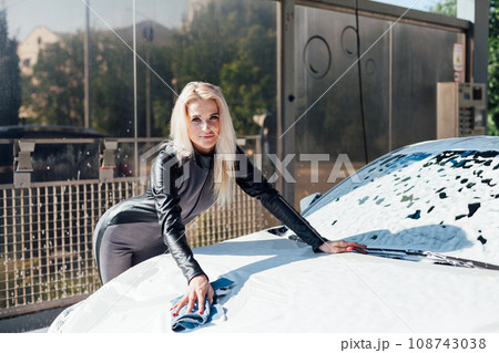 a blonde woman washes a car at a car wash clean car water in a hose for a car 108743038