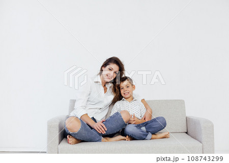 mother and son sitting on the couch in a white room 108743299