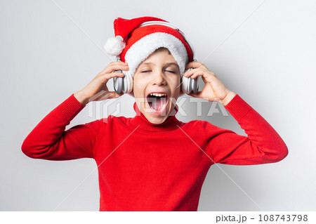 Child boy holds listening to Christmas music with funny Santa Claus hat on white background 108743798
