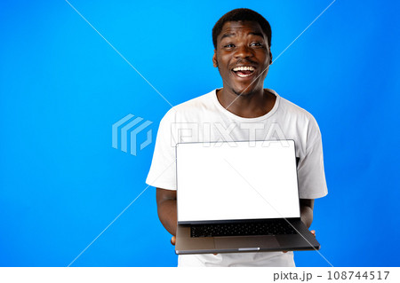Young african man holding laptop against blue background Young african man holding laptop against blue background 108744517