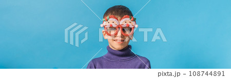 Banner Cute little child boy in party Christmas Santa Claus glasses on blue background. Kid with snow on head copy space and mockup Banner Cute little child boy in party Christmas Santa Claus glasses on blue background. Kid with snow on head copy space and mockup 108744891