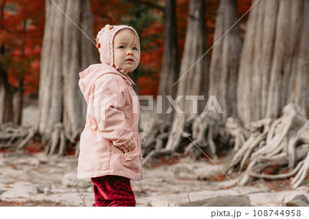 Child girl walking in a autumnal park. Little girl in warm clothes walking in the park Child girl walking in a autumnal park. Little girl in warm clothes walking in the park 108744958