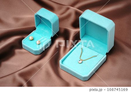 Golden necklace and earrings in blue jewelry boxes on brown silk background 108745169