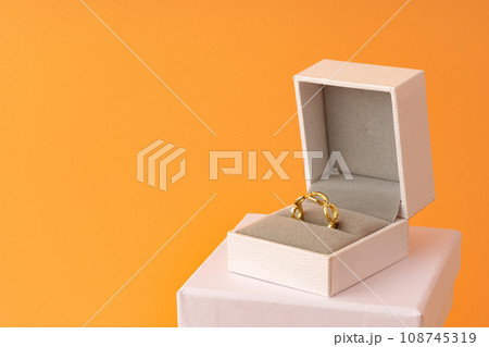 Golden ring in white jewelry box on yellow background Golden ring in white jewelry box on yellow background 108745319