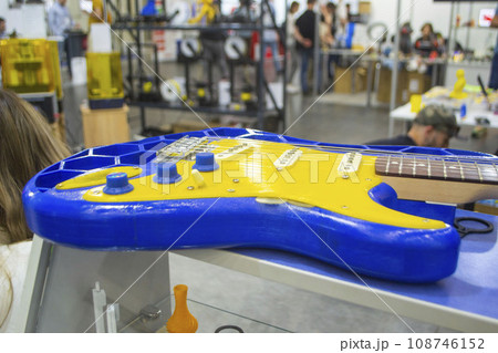 Musical instrument guitar 3D printed from molten plastic in yellow and blue colors. Part of guitar created by 3D printing from yellow-blue plastic. Concept 3D printer 3D printing modeling prototyping Musical instrument guitar 3D printed from molten plastic in yellow and blue colors. Part of guitar created by 3D printing from yellow-blue plastic. Concept 3D printer 3D printing modeling prototyping 108746152