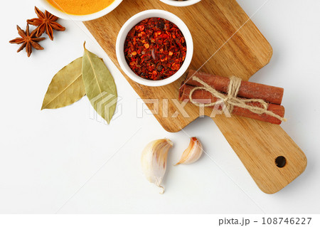 Bowls with spices on wooden board on white background Bowls with spices on wooden board on white background 108746227