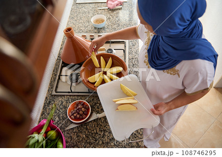 View from above of Arabian Muslim woman housewife stacking slices of organic potato, cooking traditional tagine at home View from above of Arabian Muslim woman housewife stacking slices of organic potato, cooking traditional tagine at home 108746295