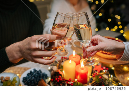 Close-up hands shot of unrecognizable happy gathering family clinking glasses with champagne, celebrating xmas, new year or birthday party, sitting at holiday dinner table with candles Close-up hands shot of unrecognizable happy gathering family clinking glasses with champagne, celebrating xmas, new year or birthday party, sitting at holiday dinner table with candles 108746926