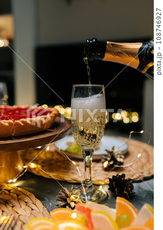 Vertical cropped shot of unrecognizable man pouring champagne into glass at dinner feast table during family party on blurred background bokeh lights. Concept of preparation to holiday celebration. 108746927