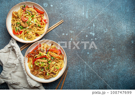 Two bowls with Chow Mein or Lo Mein, traditional Chinese stir fry noodles with meat and vegetables, served with chopsticks top view on rustic blue concrete background, space for text Two bowls with Chow Mein or Lo Mein, traditional Chinese stir fry noodles with meat and vegetables, served with chopsticks top view on rustic blue concrete background, space for text 108747699