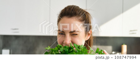 Portrait of beautiful woman cooking, holding fresh parsley, adding herbs while making salad, healthy meal in the kitchen 108747994