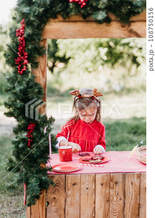 Christmas in july. Child waiting for Christmas in wood in july. portrait of little girl drinking hot cocoa with marshmallow and gingerBread man cookies. Merry Christmas and Happy Holidays. Christmas in july. Child waiting for Christmas in wood in july. portrait of little girl drinking hot cocoa with marshmallow and gingerBread man cookies. Merry Christmas and Happy Holidays. 108750156