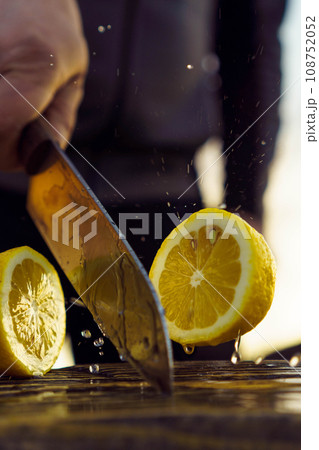 Adult man cutting lemon in half with knife. Human separate into pieces juicy and sour fruit that lie on table. Adult man cutting lemon in half with knife. Human separate into pieces juicy and sour fruit that lie on table. 108752052