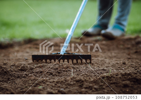 Garden rake in hands of human loosening ground, standing on grass. Soil treatment using agricultural object in spring. Garden rake in hands of human loosening ground, standing on grass. Soil treatment using agricultural object in spring. 108752053