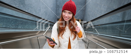 Portrait redhead girl tourist, goes up stairs with smartphone, follows route on mobile phone app, holds backpack and smiles 108752514
