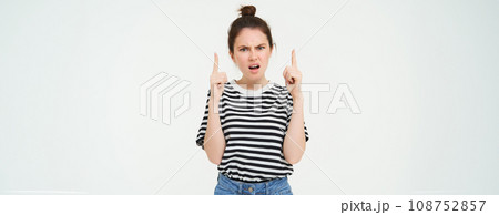 Portrait of angry, frowning woman, arguing and pointing fingers up, stands over white background 108752857