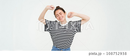 Portrait of woman feeling pleased after good nap, stretching arms and smiling, standing over white background Portrait of woman feeling pleased after good nap, stretching arms and smiling, standing over white background 108752938