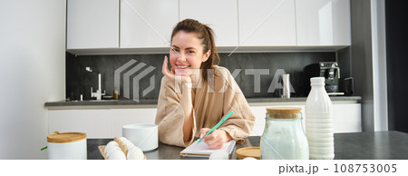 Attractive young cheerful girl baking at the kitchen, making dough, holding recipe book, having ideas Attractive young cheerful girl baking at the kitchen, making dough, holding recipe book, having ideas 108753005
