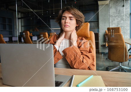 Portrait of female entrepreneur, manager sits in office with laptop, massages, touches neck, feels tension in muscles Portrait of female entrepreneur, manager sits in office with laptop, massages, touches neck, feels tension in muscles 108753100
