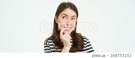 Portrait of curious young woman, bites her finger and looks up thoughtful, thinking, makes decision, choosing smth to eat, stands over white background 108753252