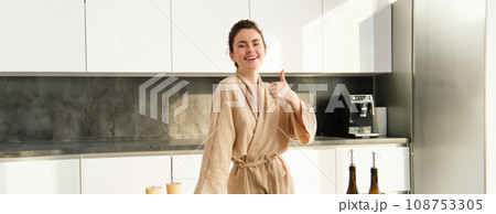 Portrait of happy young woman preparing vegetarian dinner, showing thumbs up, wife cooking in kitchen and smiling, recommending product, chopping vegetables for healthy salad 108753305